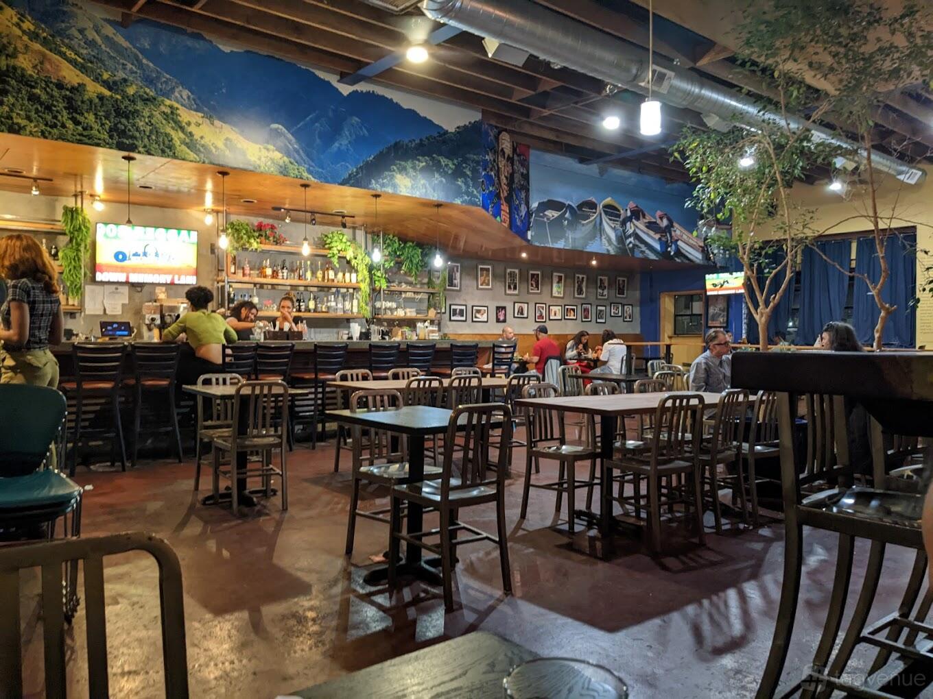 A restaurant with mural-covered walls, exposed ceiling beams, and a bar with framed photos at Kingston 11 Cuisine.