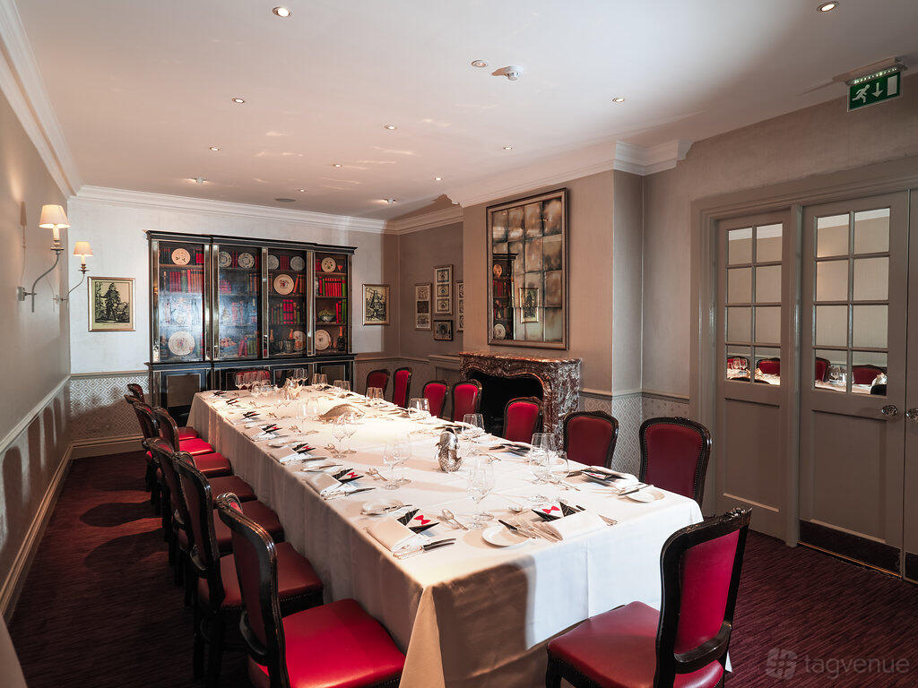 A dining room with a long table, red upholstered chairs, and a china cabinet at Mosimann's.
