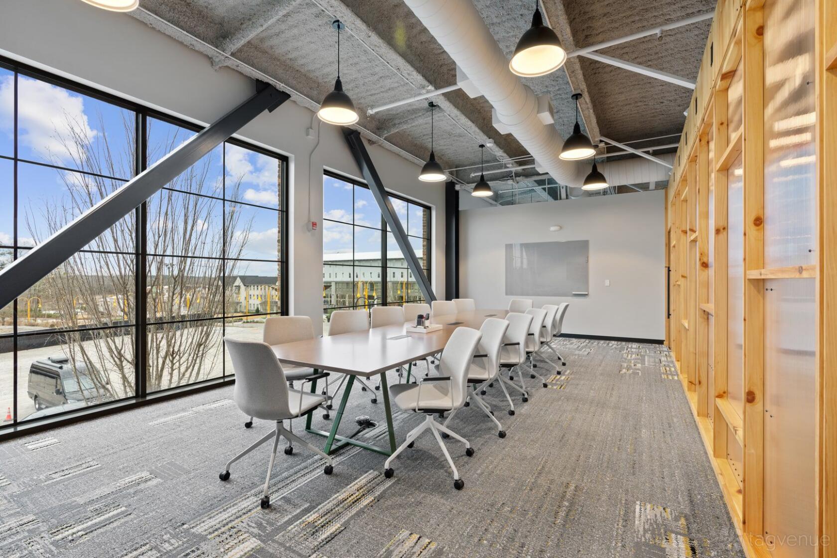 A boardroom with a long white conference table, ergonomic chairs, and floor-to-ceiling windows at ROAM AT TRILITH.