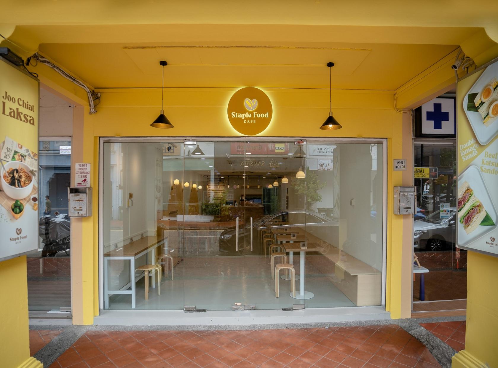 A café with yellow walls, hanging pendant lights, and glass frontage at Staple Food Cafe.