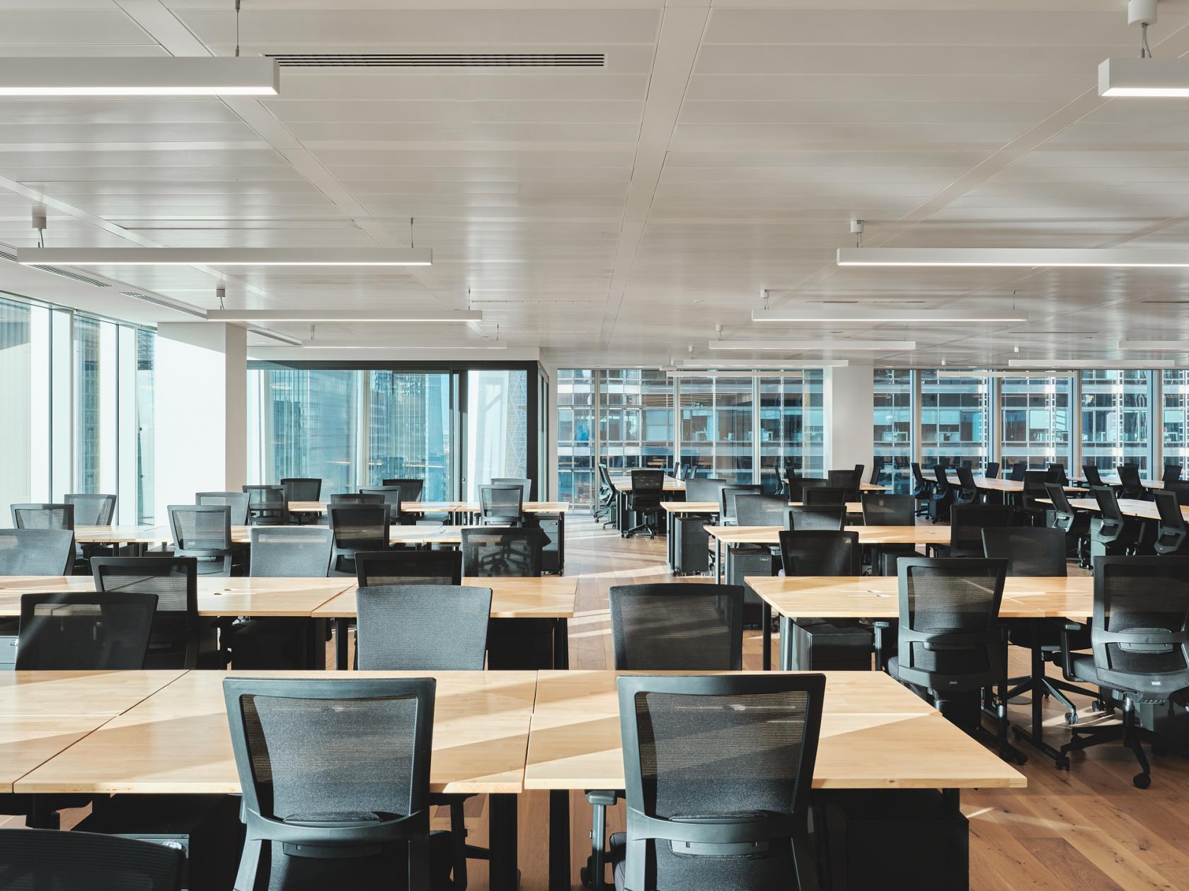 An event venue with rows of wooden tables, black chairs, and floor-to-ceiling windows at Churchill Place.