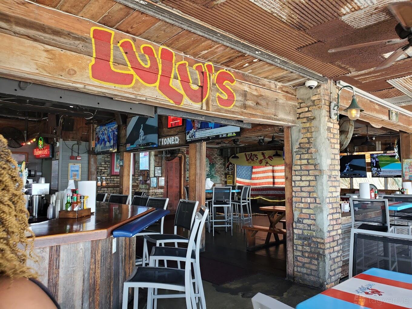 A casual bar with rustic wood beams, exposed brick walls, bar seating, and American flag decor at Lulu's Bait Shack.