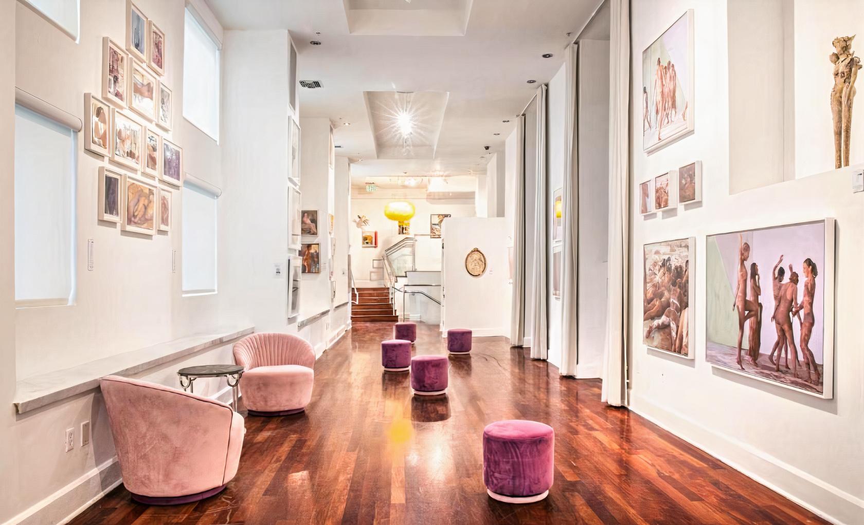 A gallery with hardwood floors, white walls adorned with artwork, and pink velvet chairs at The Sagamore Hotel.