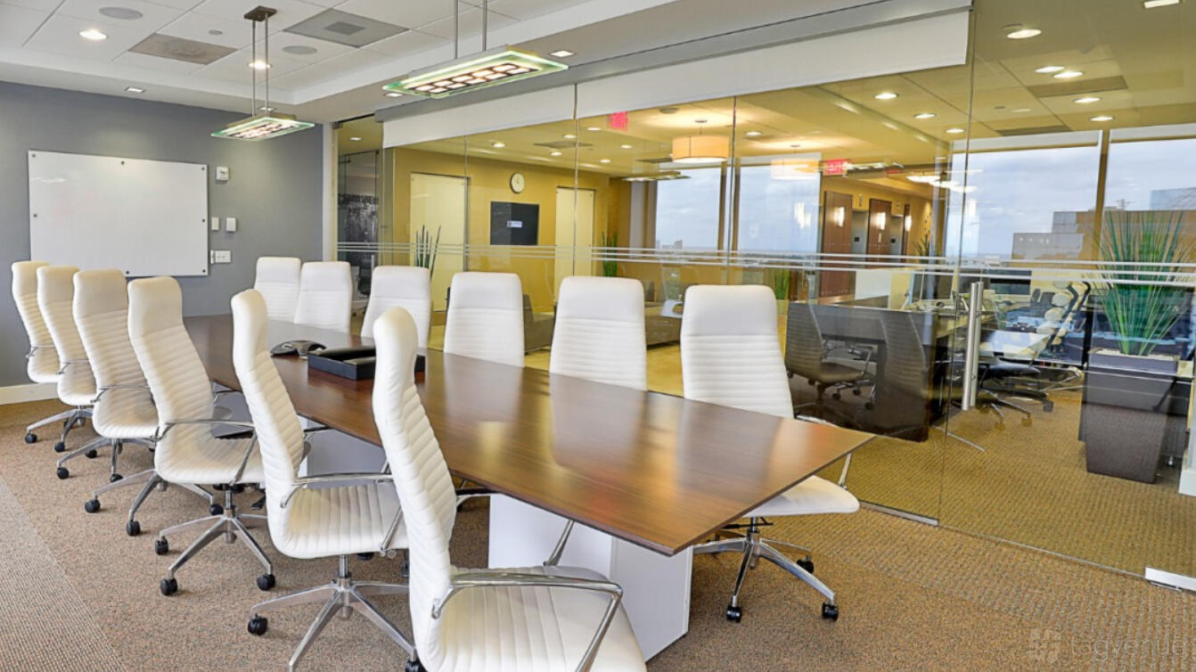 A meeting room with a long wooden conference table, white high-back chairs, and glass walls at Empire Executive Offices, Fort Lauderdale.