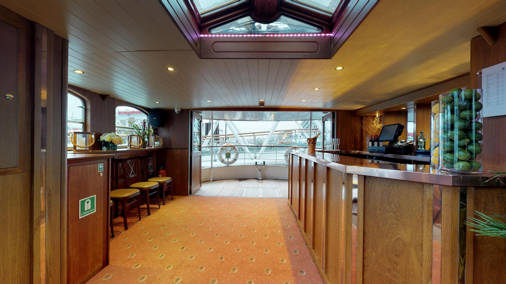 A boat venue with a wood-paneled interior, carpeted floor, skylight, and riverside views at Edwardian - Thames Luxury Charters.