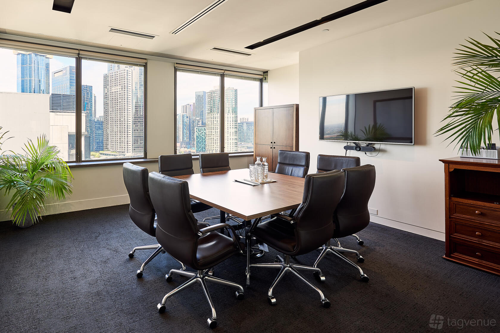 A meeting room with a large window, city views, dark carpet, and a wall-mounted screen at The Cluster.