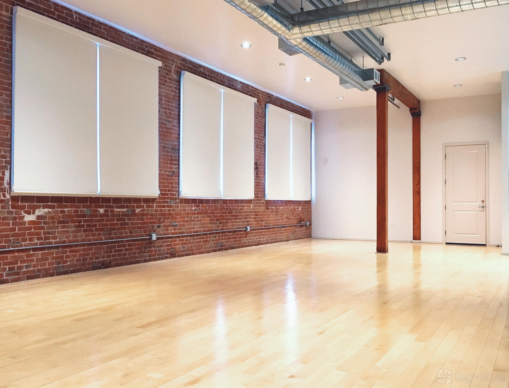 A photo studio with exposed brick walls, large ceiling pipes, and light wood floors at Mick Jones Studio.