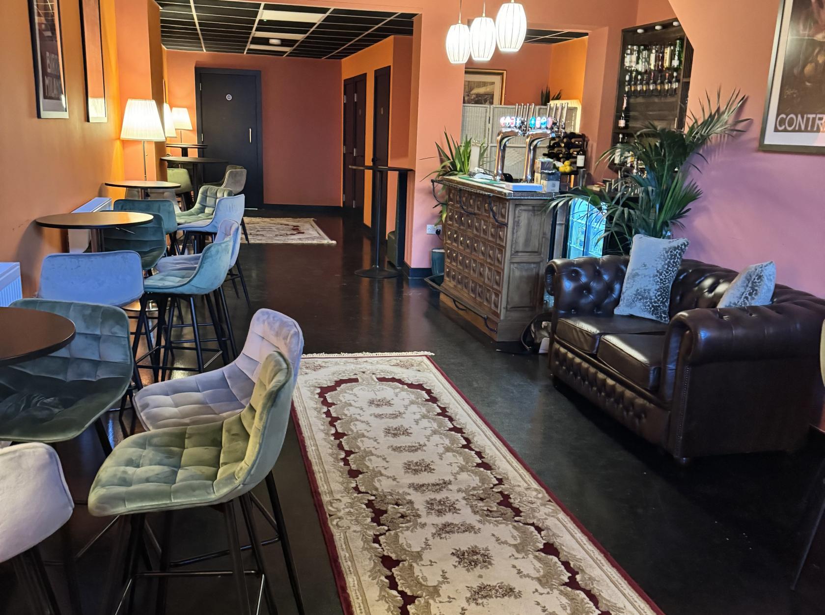 A bar with velvet chairs, round tables, a vintage leather sofa, and patterned rug at 222 Railton Private Hire Bar.