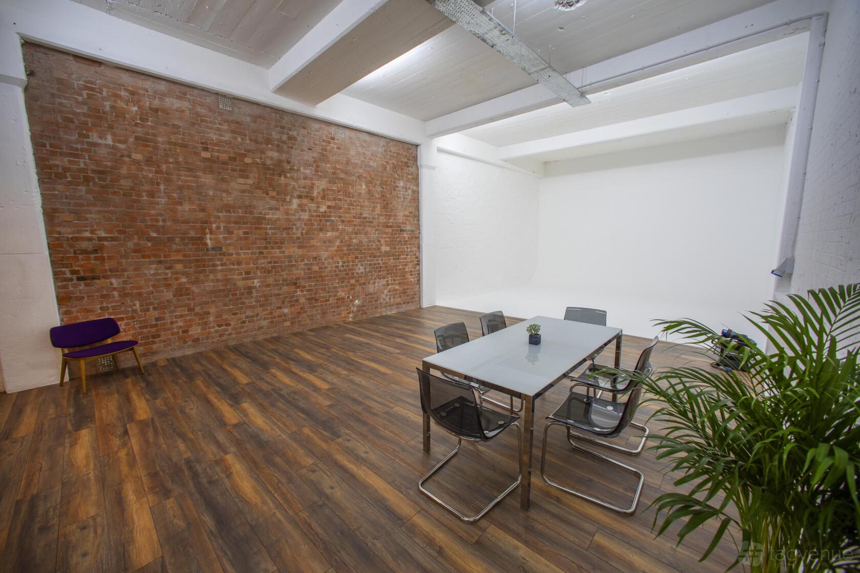 A meeting room with a brick accent wall, wood floors, and a glass table with chairs at Tower Bridge Studios.