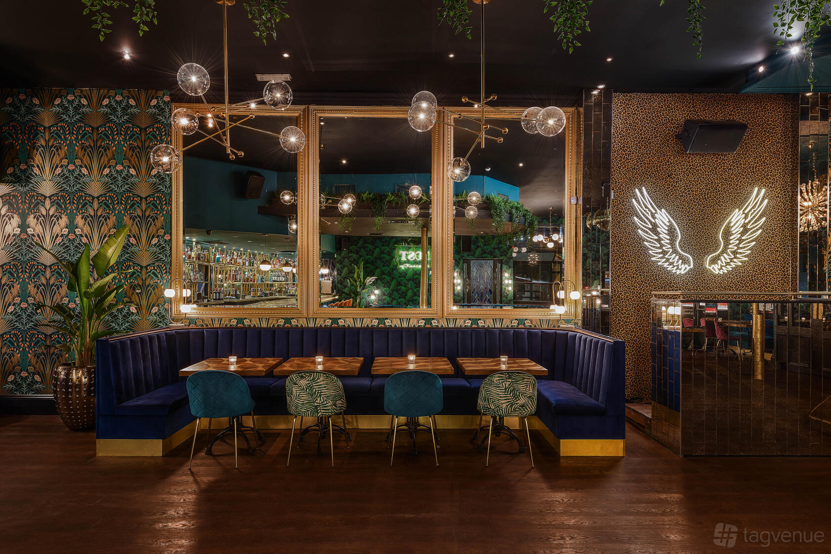 A cocktail bar with velvet banquette seating, globe pendant lights, and tropical patterned wallpaper at Lost Society.