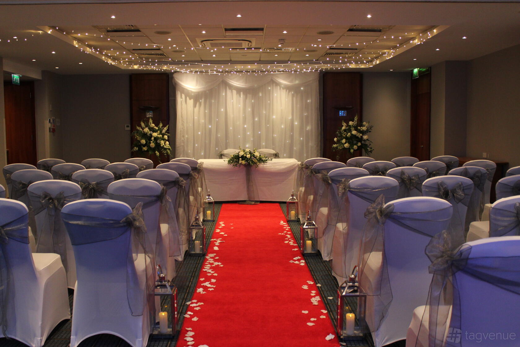 An event space with a red aisle runner, white chair covers, and fairy lights at Holiday Inn London Bexley