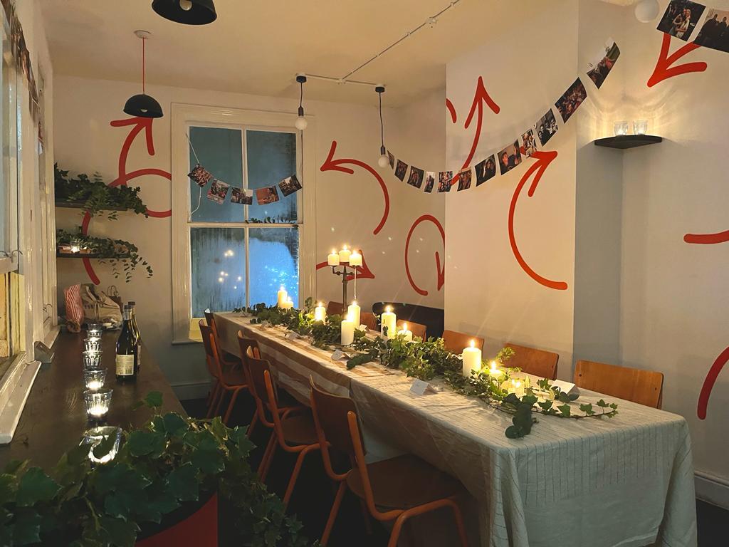 An intimate event space with a long table, draped greenery, candles, and photo garlands on the wall at Trampoline.