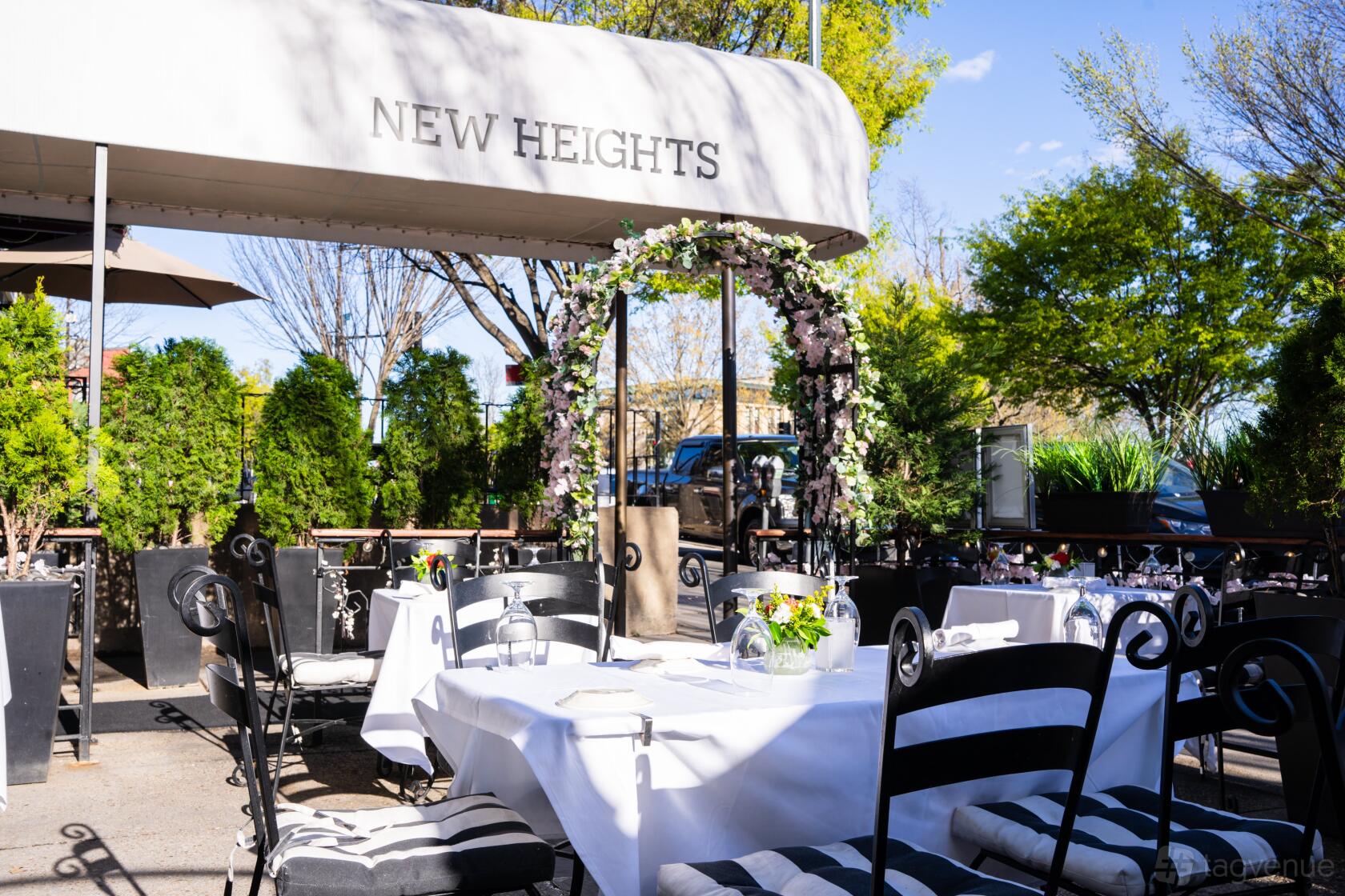 A restaurant terrace with white tablecloths, floral arch, and greenery at New Heights Restaurant.