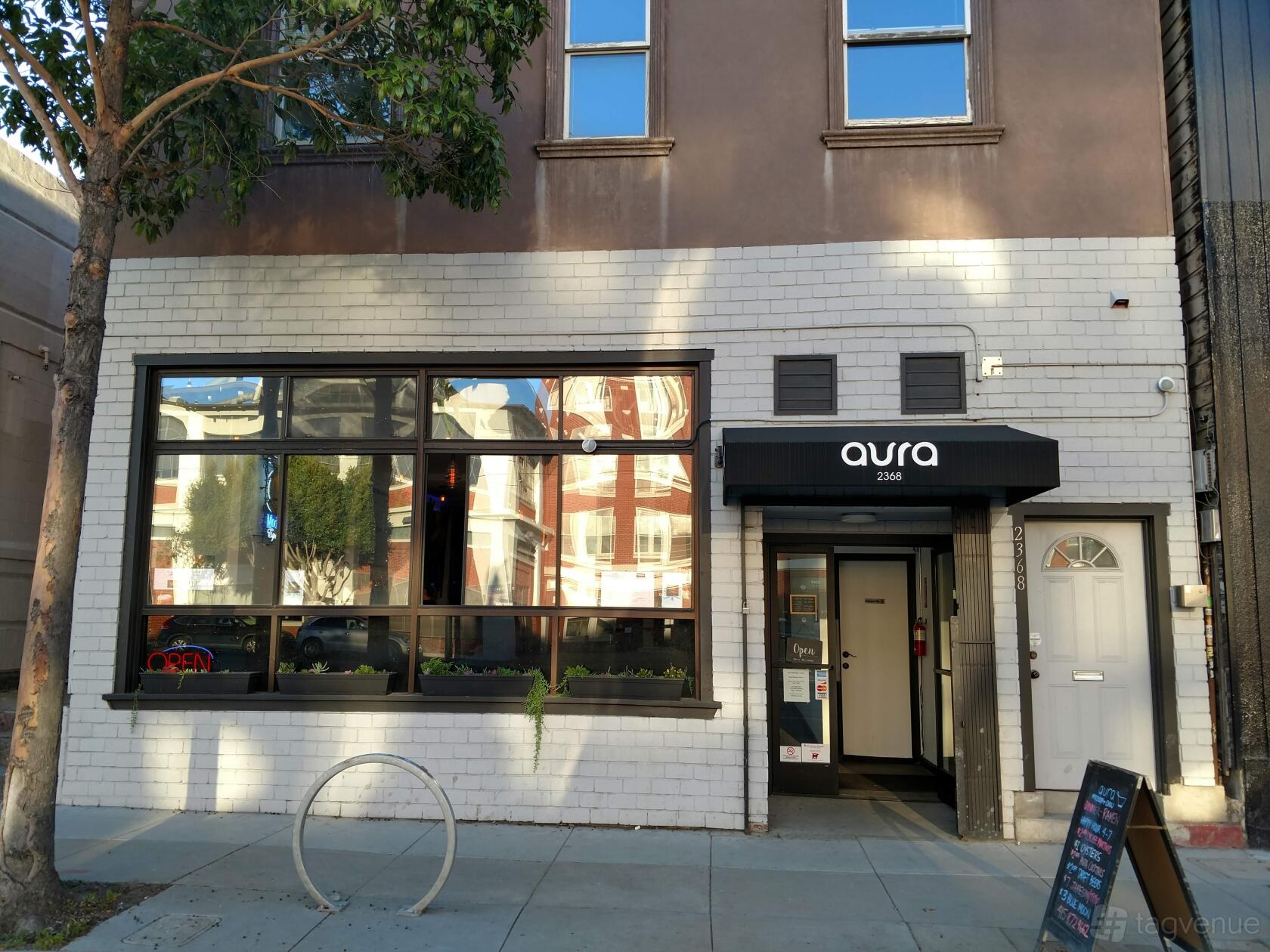 A pub with a white brick facade, large windows, and a black awning displaying 'aura' at Aura Cinema.