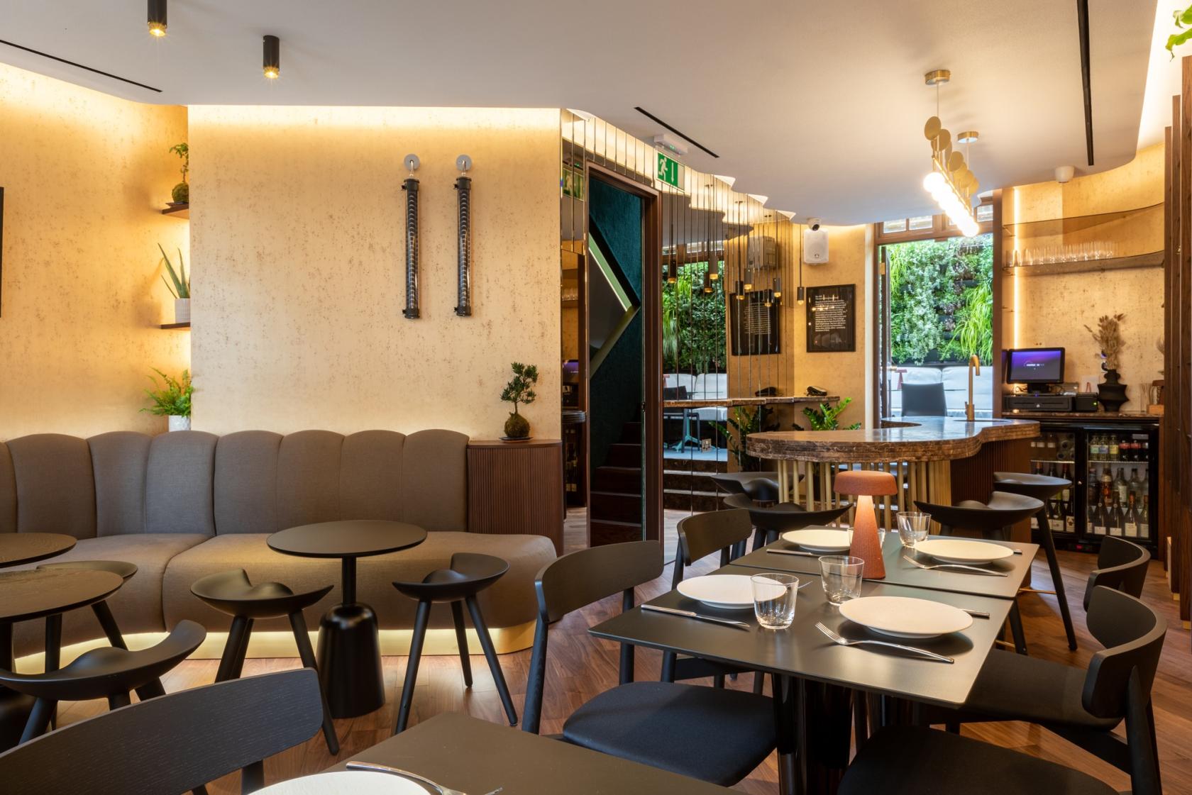 A restaurant with taupe banquette seating, round black tables, and warm accent lighting at Bantof.