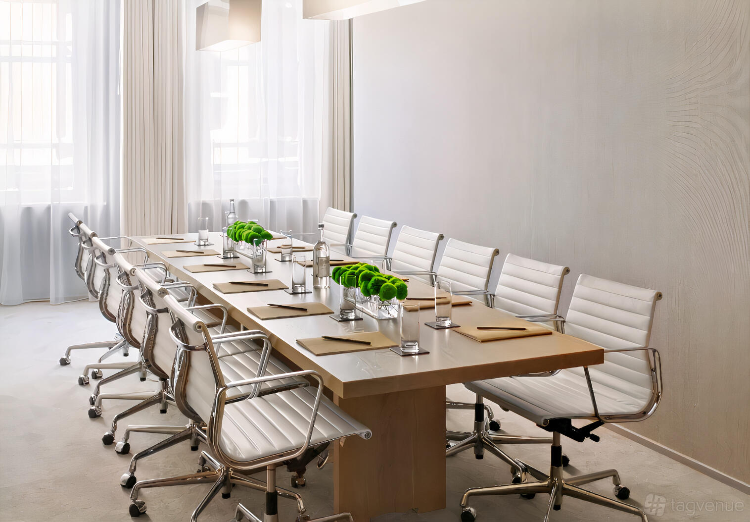 A hotel meeting room with a long wooden table, white leather chairs, and large windows at London EDITION.