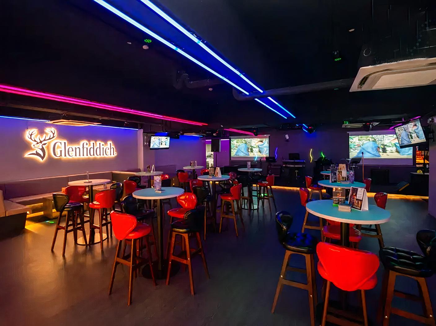 An event space with neon lighting, cocktail tables, bar stools, and multiple flat-screen TVs at Major 99 Karaoke and Entertainment Center.