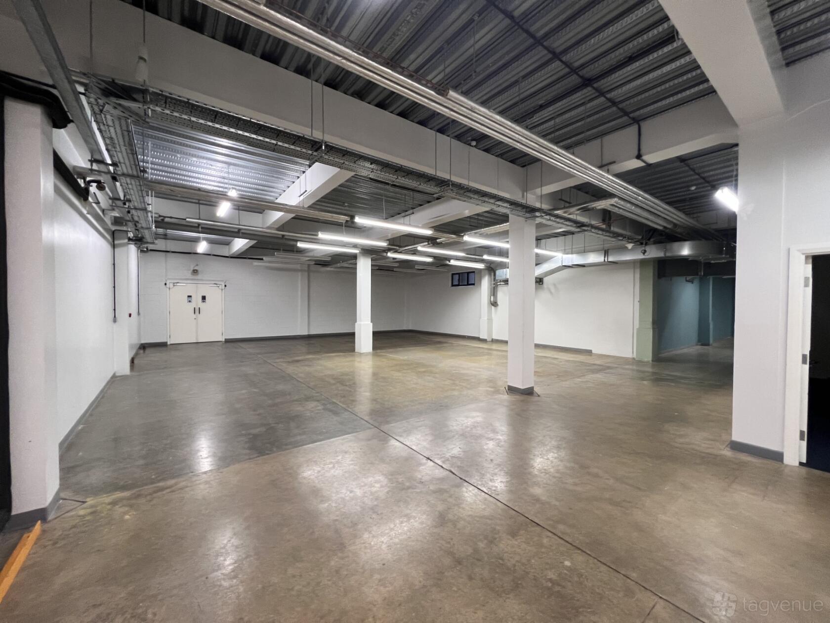 A film studio with polished concrete floors, exposed ceiling pipes, and overhead lighting at London North Studios.