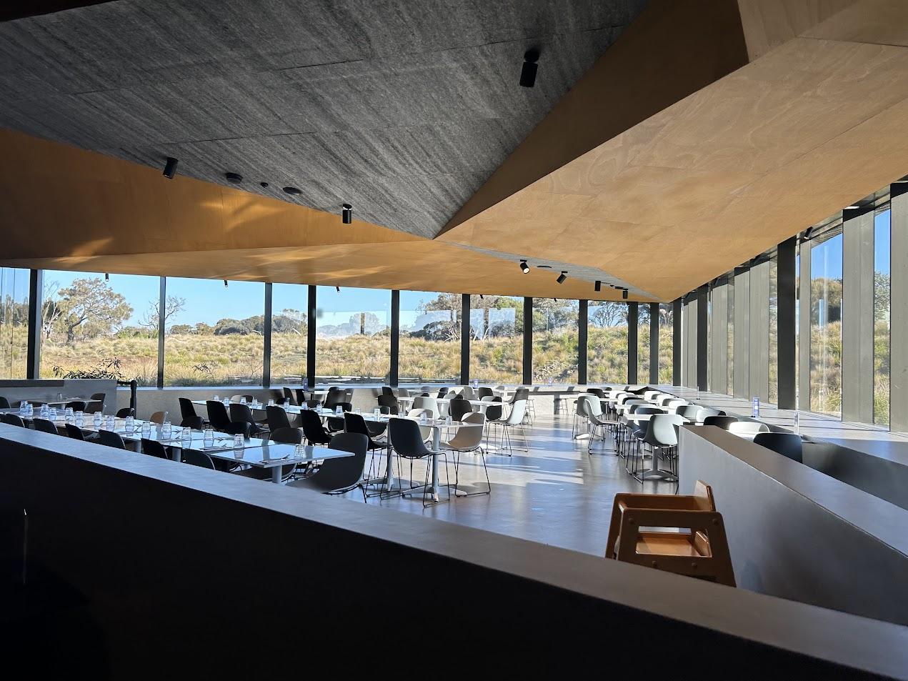 An event venue with floor-to-ceiling windows, angled wood ceilings, and black chairs at Penguin Parade Centre