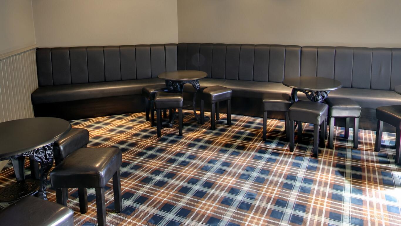 A lounge in a restaurant with black leather banquette seating, round tables, and plaid carpet at The Koyla Kitchen @ The Thorns.