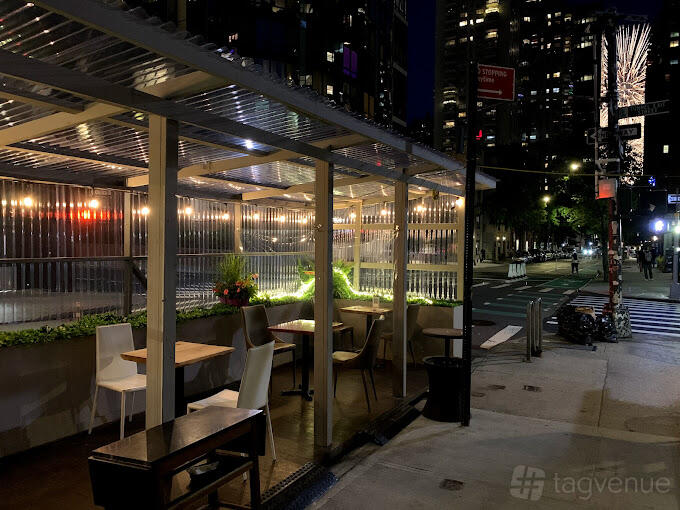 An outdoor restaurant patio with wooden tables, mixed chairs, and clear roofing at Sushi Ryusei.