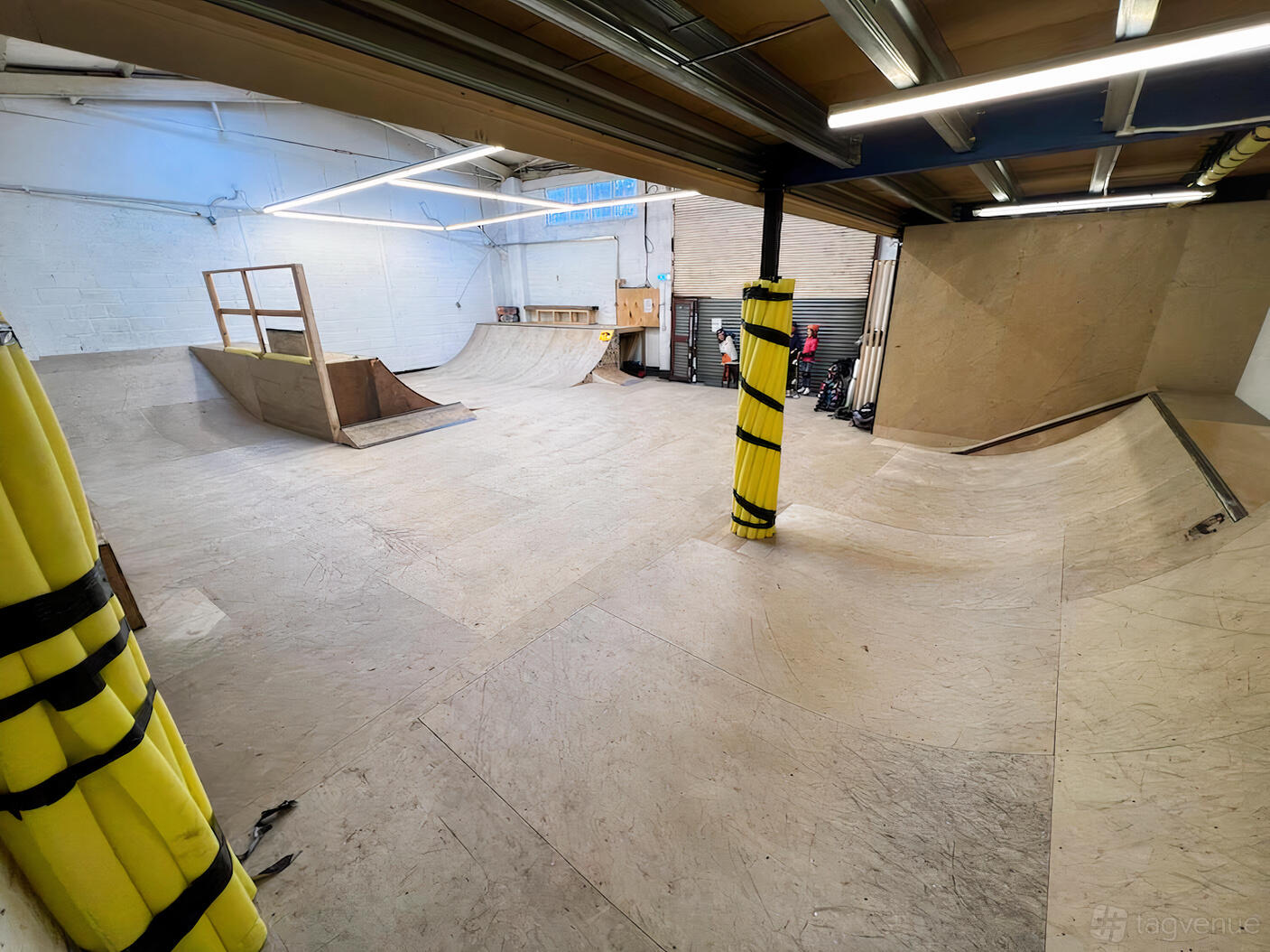 An indoor skatepark with wooden ramps, white brick walls, and yellow safety padding at School of Skate Copeland Park.