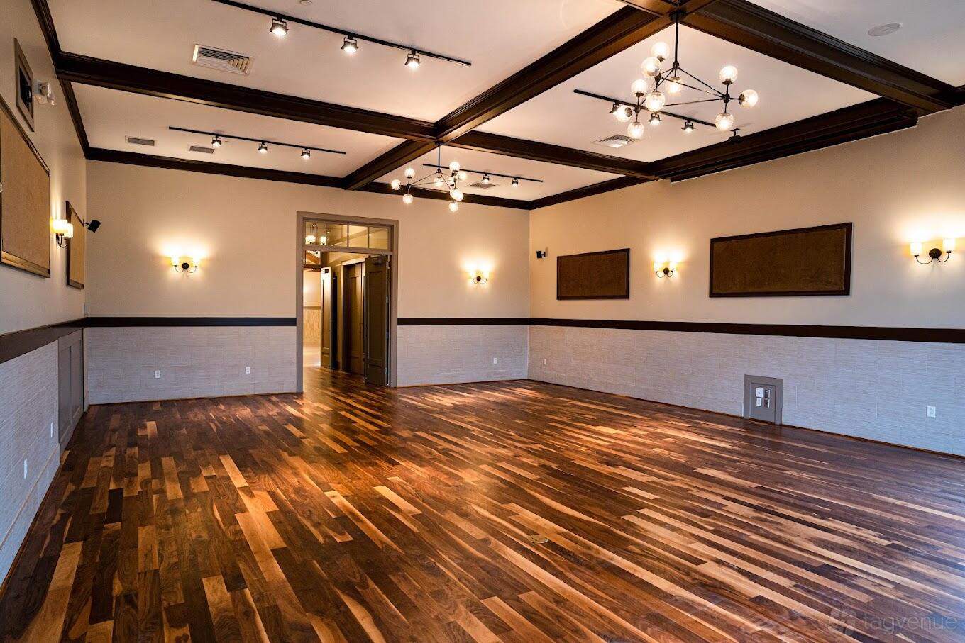 A dining room with hardwood floors, dark wood ceiling beams, and modern chandeliers at Milano Event Center.