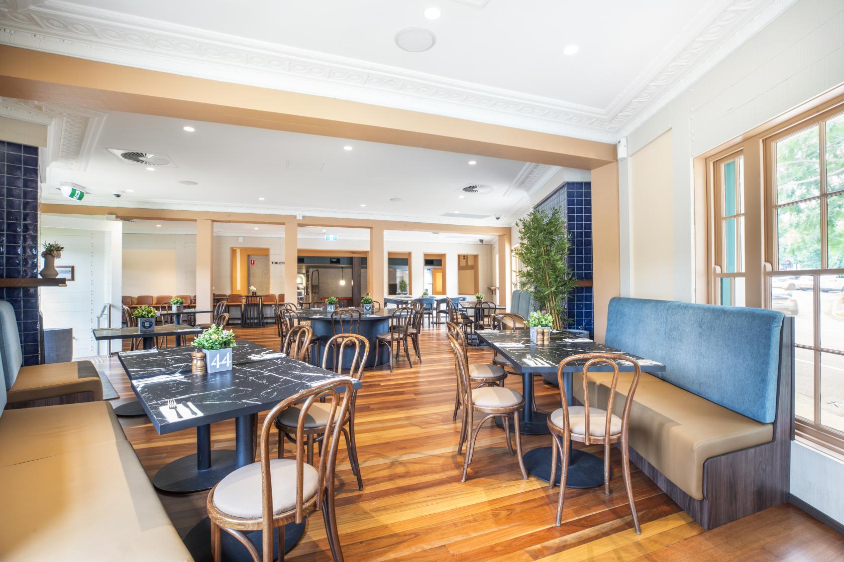 A pub with wooden floors, marble tables, blue booth seating, and potted plants at Berwick Inn Hotel.