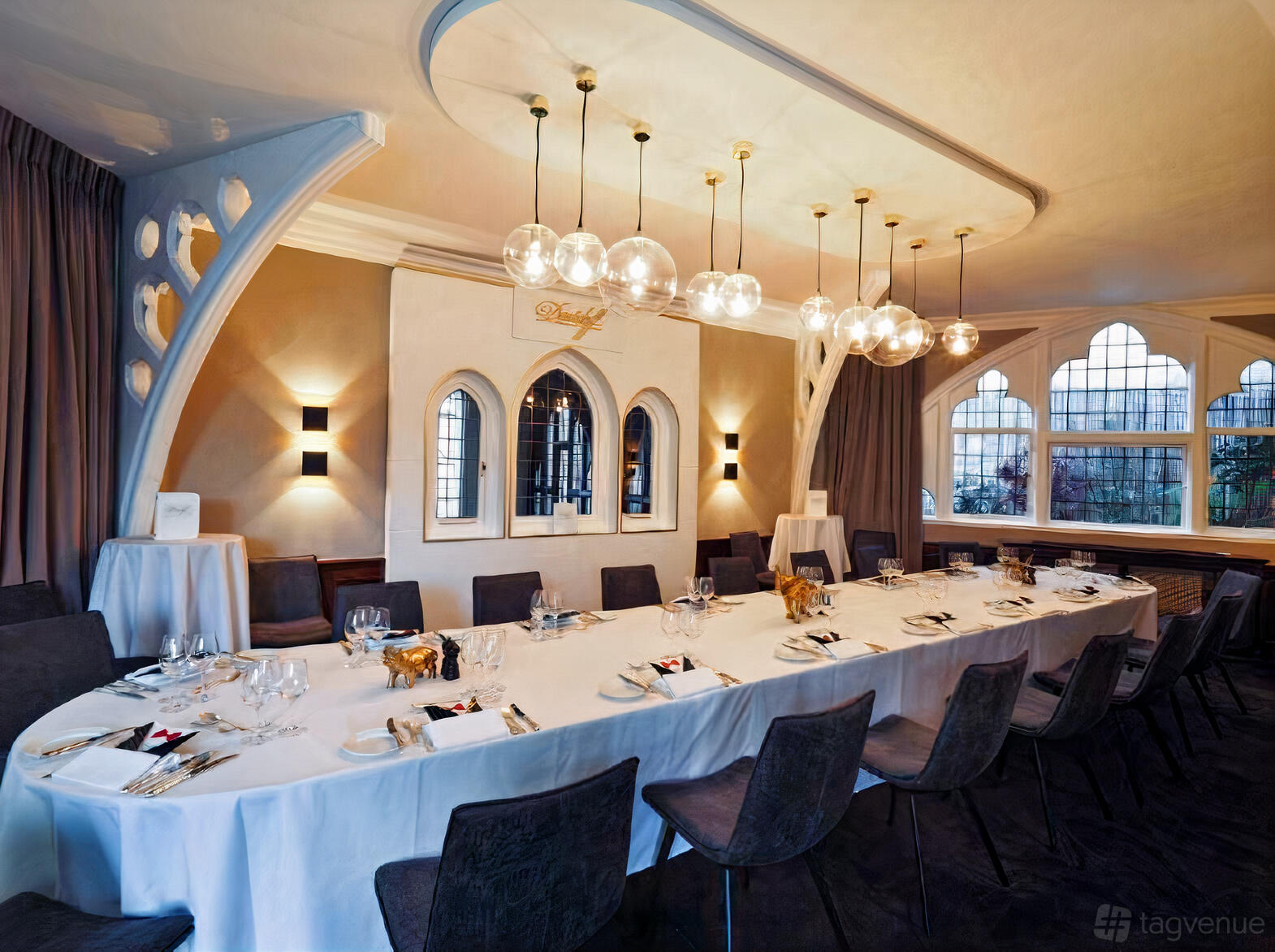 An event space with arched windows, globe pendant lights, and a long table set for dining at Mosimann's.