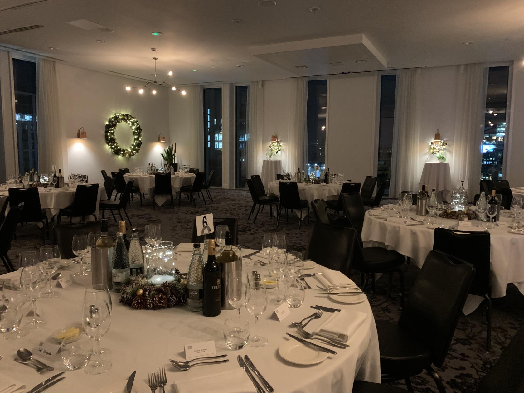 A hotel hall with round tables set for dining, floor-to-ceiling windows, and festive wreath decor at voco Manchester.