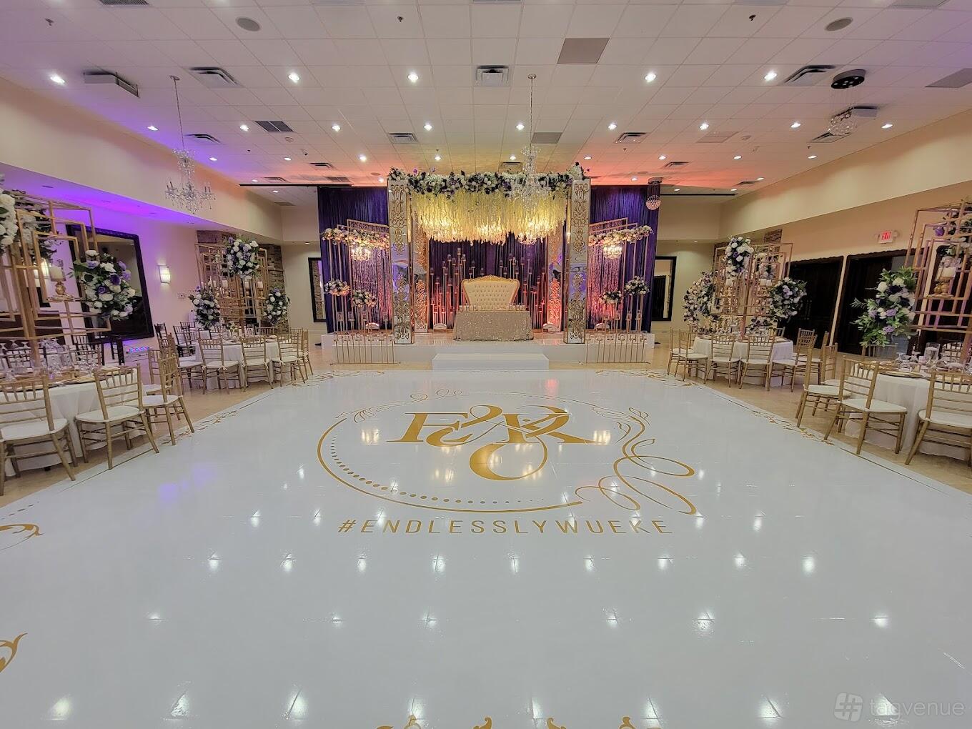 A banquet hall with a large white dance floor, floral stage backdrop, gold chairs, and decorative lighting at Palacio Maria Banquet Hall.