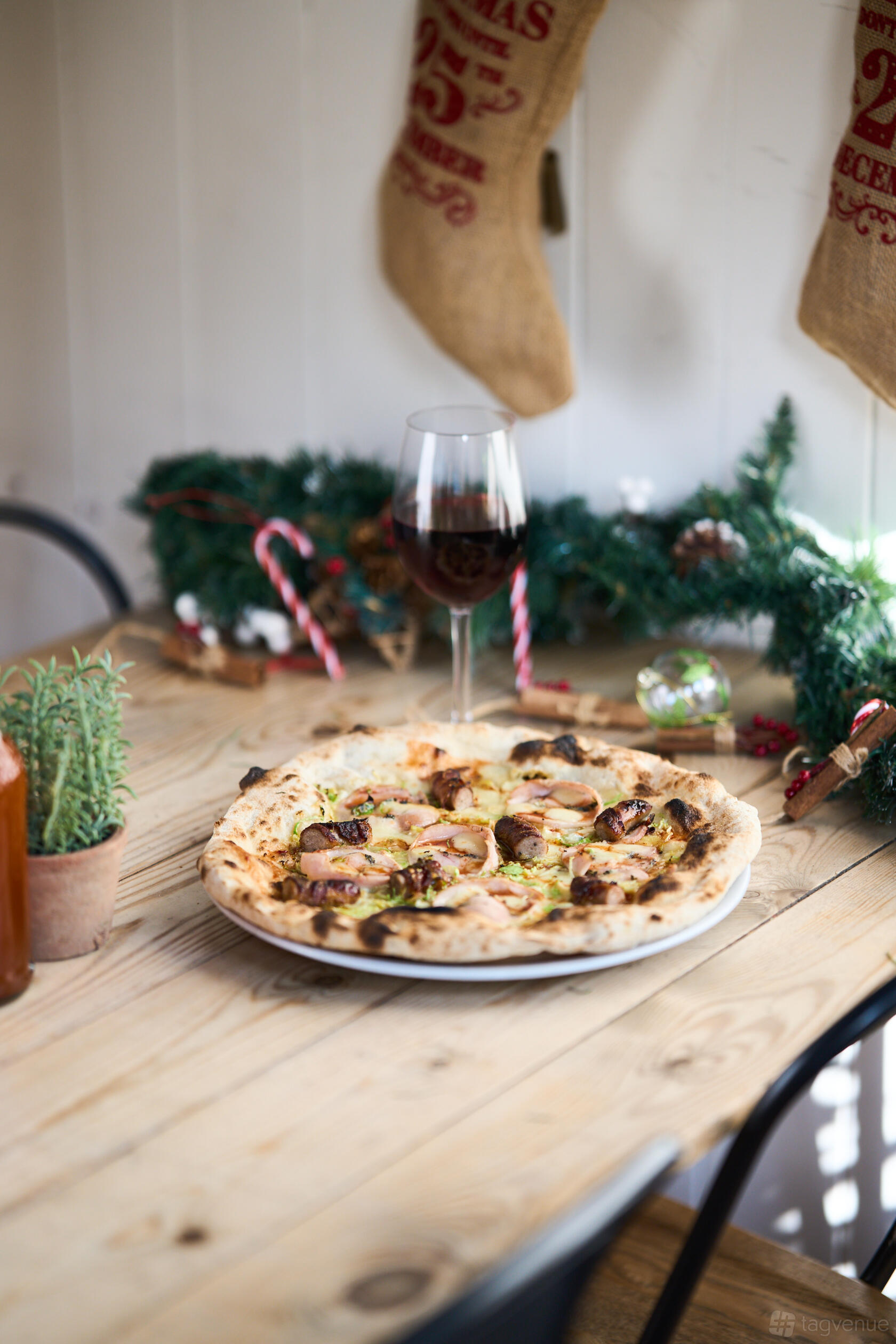 A restaurant table with a wood-fired pizza, a glass of red wine, and holiday greenery at Mamma Dough Brixton.