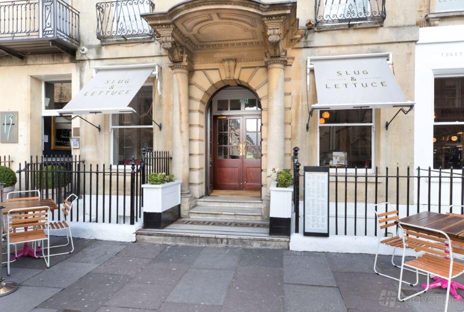 An event venue with classic stone facade, arched doorway, and outdoor seating at Slug and Lettuce Bath.
