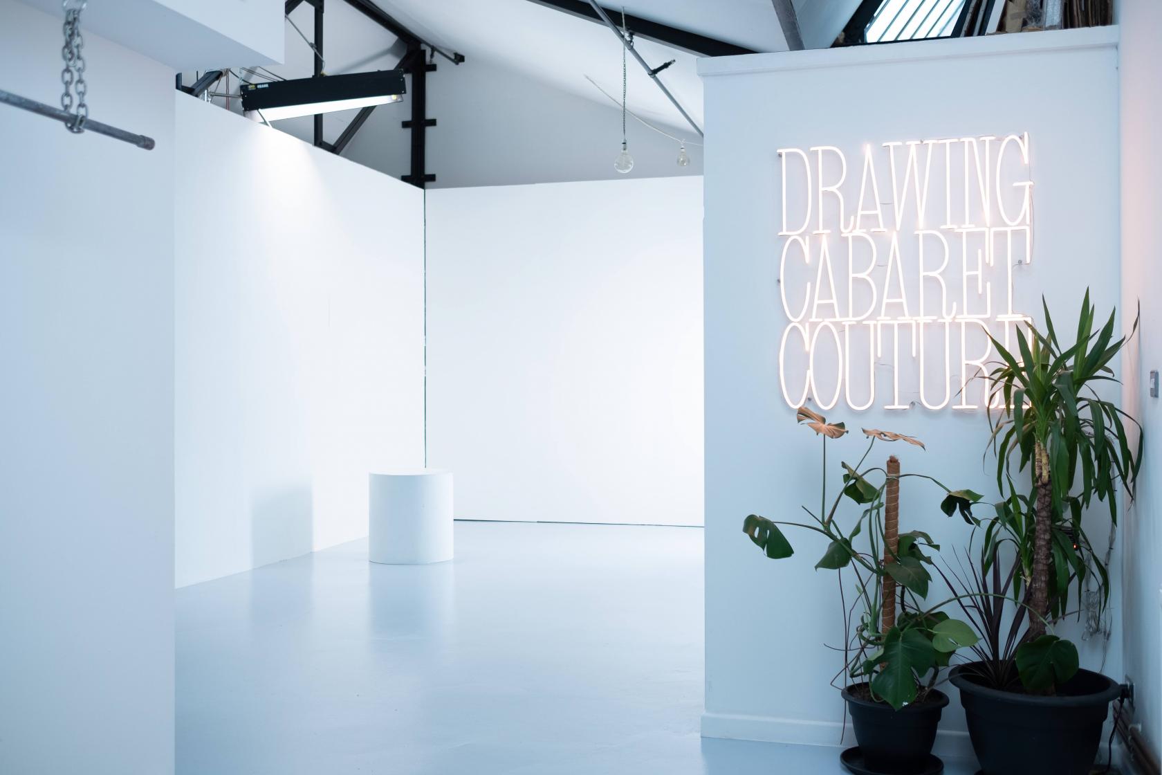 A photo and film studio with white walls, high ceilings, neon signage, and potted plants at DCC Studio Hackney Wick London.