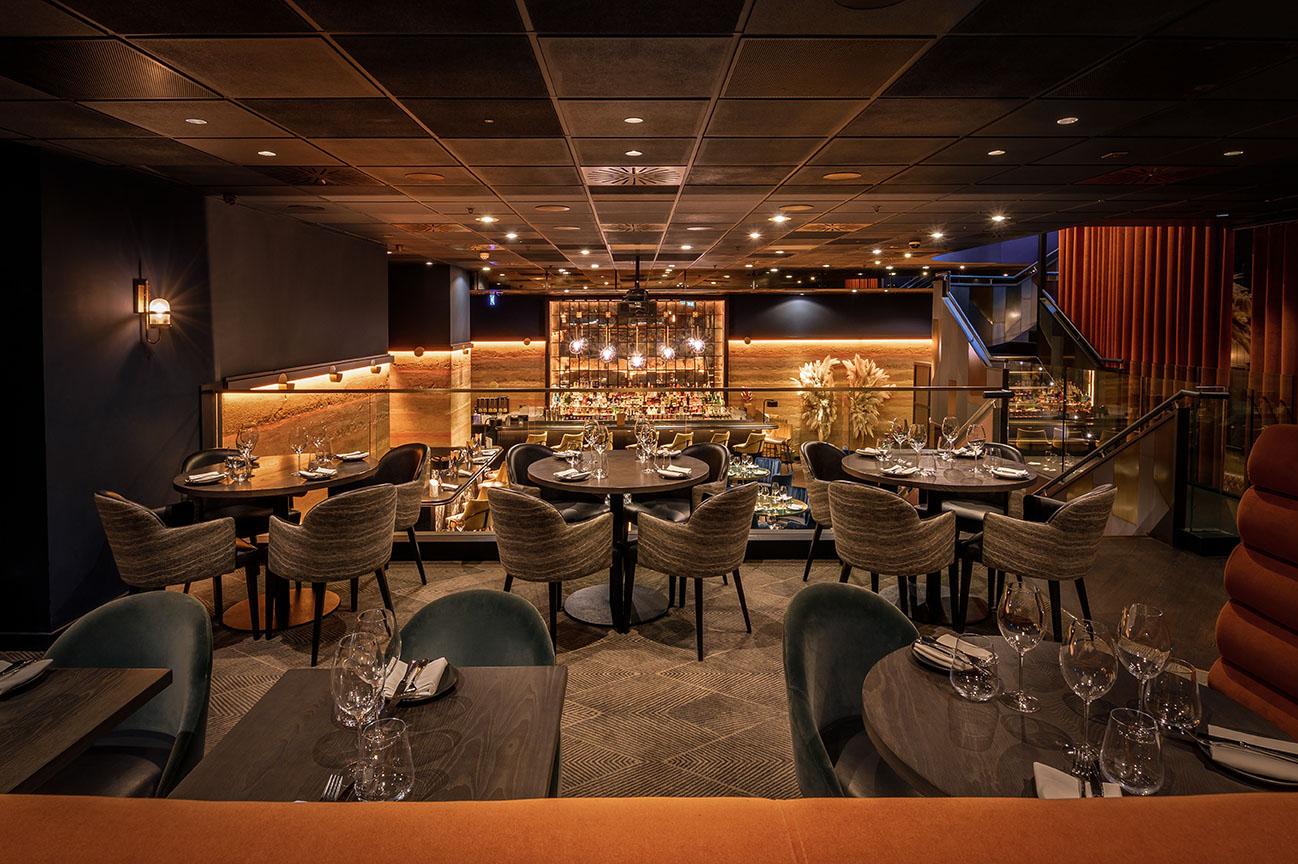 An event space in a restaurant with curved banquettes, velvet chairs, and glass railing overlooking a bar at Gaucho Charlotte Street.
