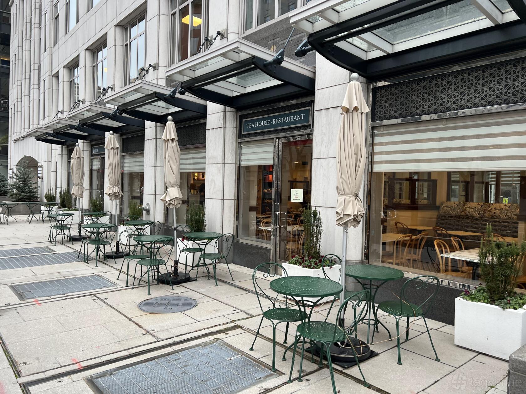 A restaurant with green metal patio tables, chairs, and closed umbrellas outside Teaism Lafayette Park.