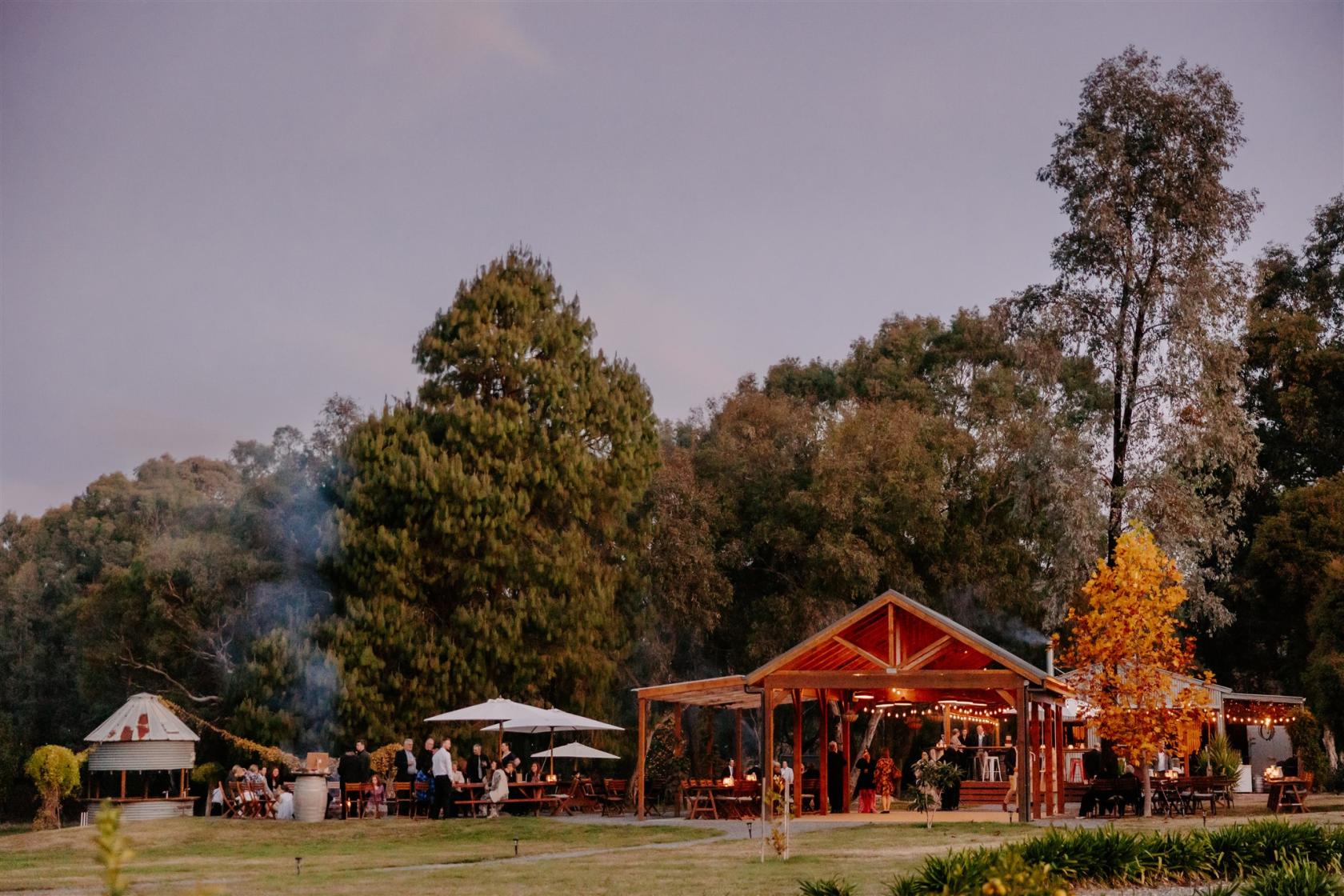 An outdoor microbrewery with a wooden pavilion, string lights, and seating areas surrounded by trees at Bonfire Station Microbrewery.