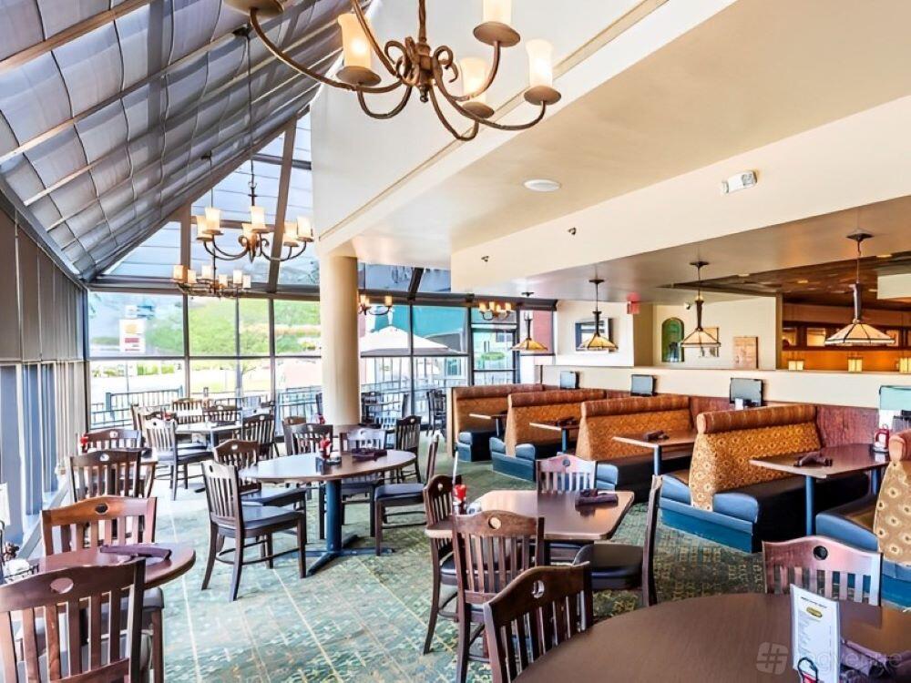 A function room in a restaurant with round wooden tables, cushioned booths, and large windows at O'Malley's - Sterling.