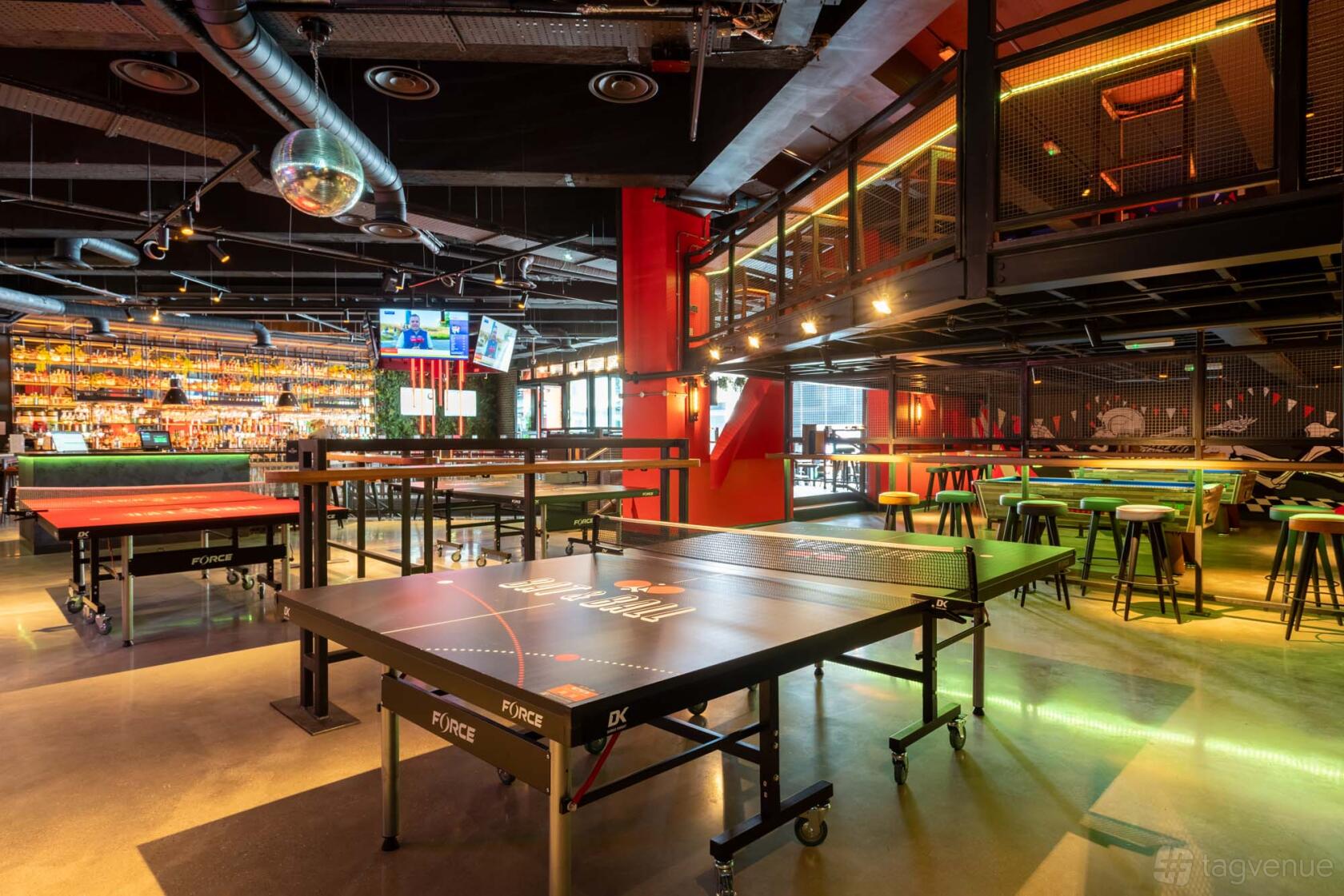 An event space in a bar with several ping pong tables, high stools, and a well-stocked bar at Bat & Ball.
