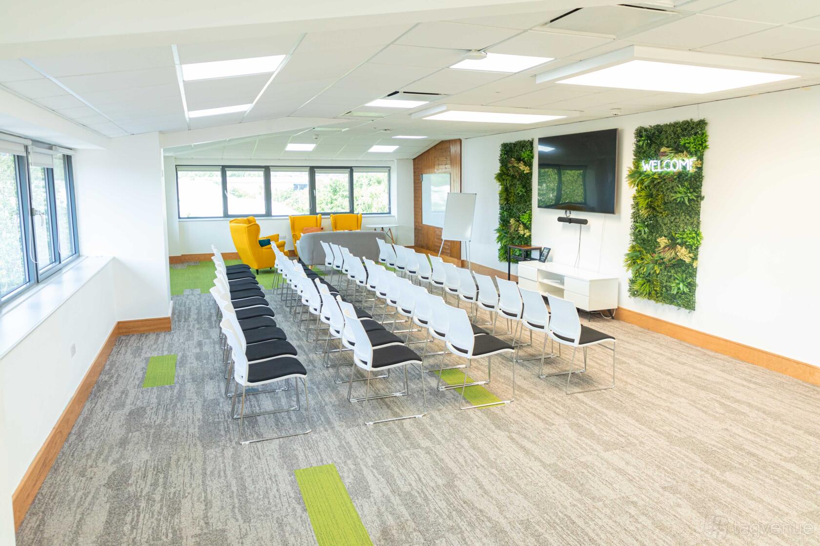 A training room with rows of black and white chairs, green accent panels, a wall-mounted screen, and large windows at Hope Park Workspaces, City Gateway.