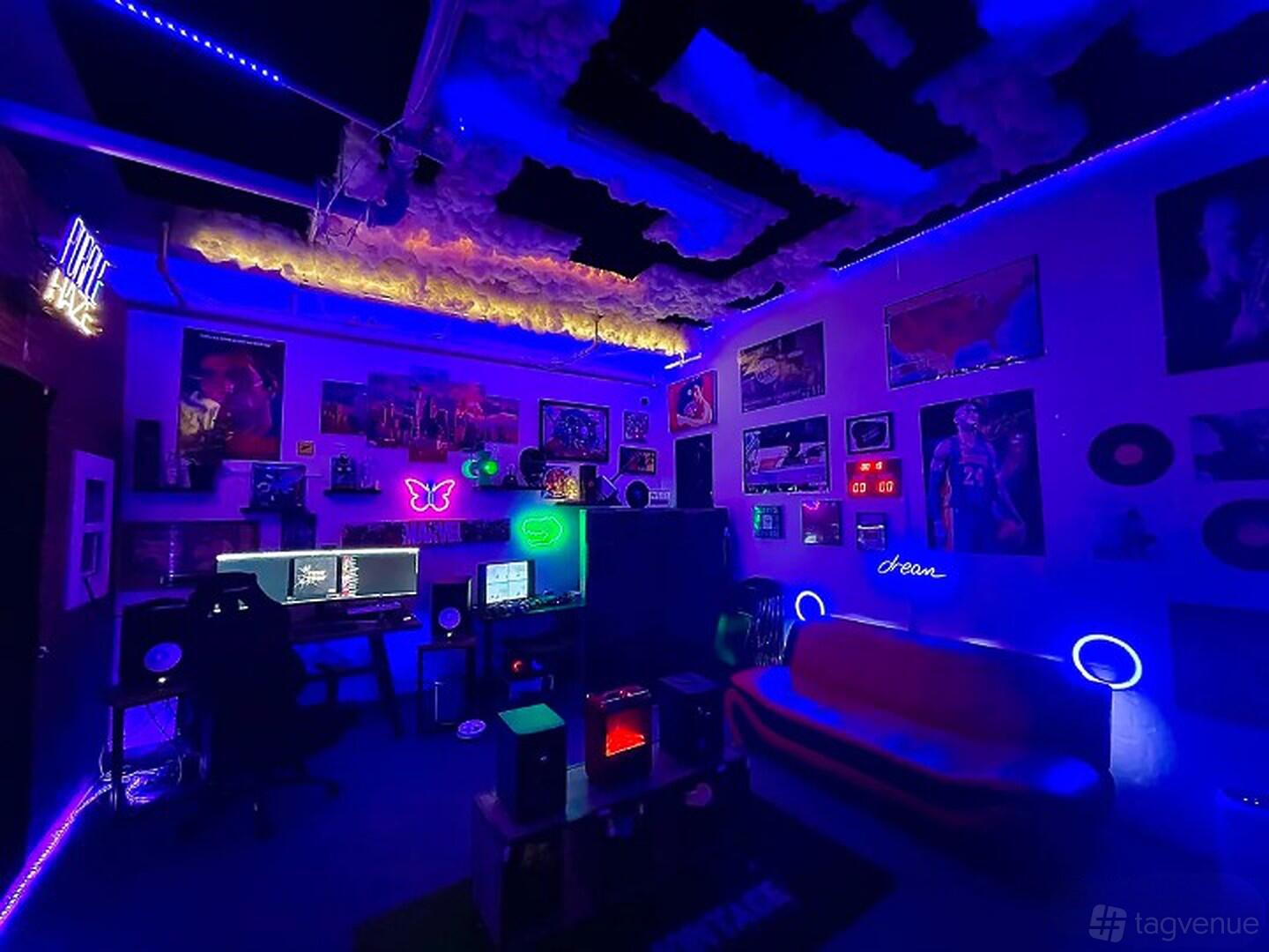 A recording studio with neon lighting, soundproofed ceiling panels, wall art, and a workstation at Club122 Studio.