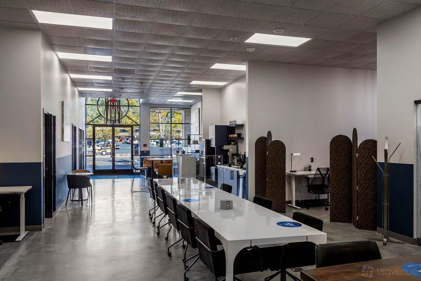 An event space with a long white table, modern chairs, and large windows letting in natural light at Pillar Cowork.