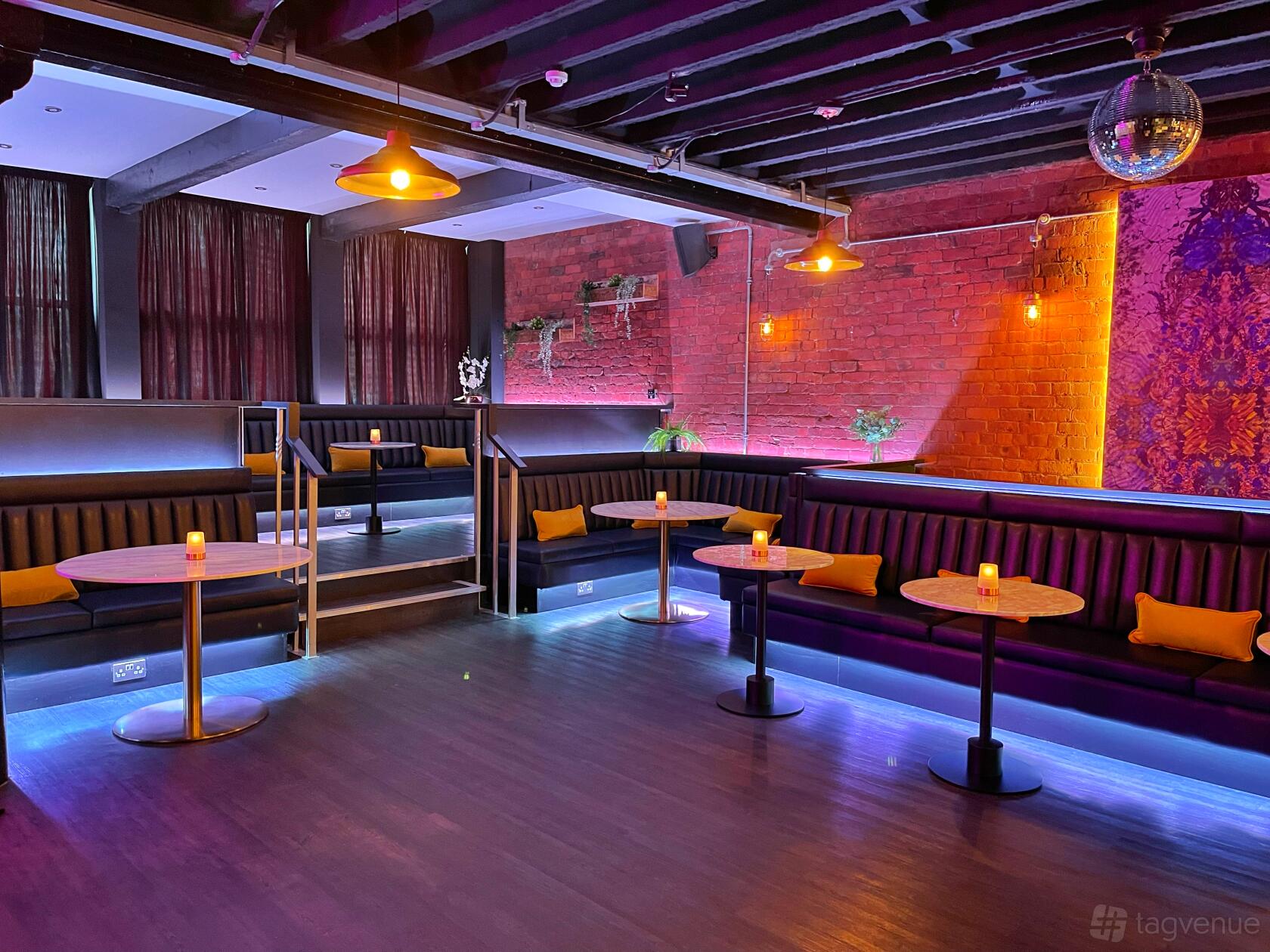 An event space in a hotel with exposed brick walls, banquette seating, round tables, and moody lighting at Velvet Hotel, Bar & Brasserie.