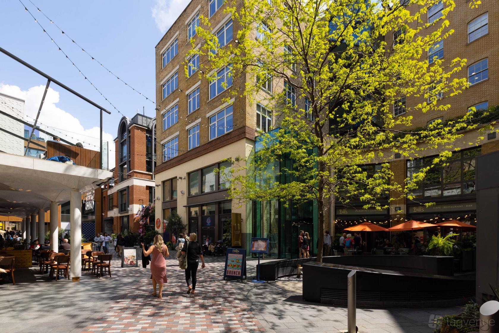 An office building with outdoor seating, string lights, and a tree-lined walkway at Rivvia Pronto Meeting Rooms.