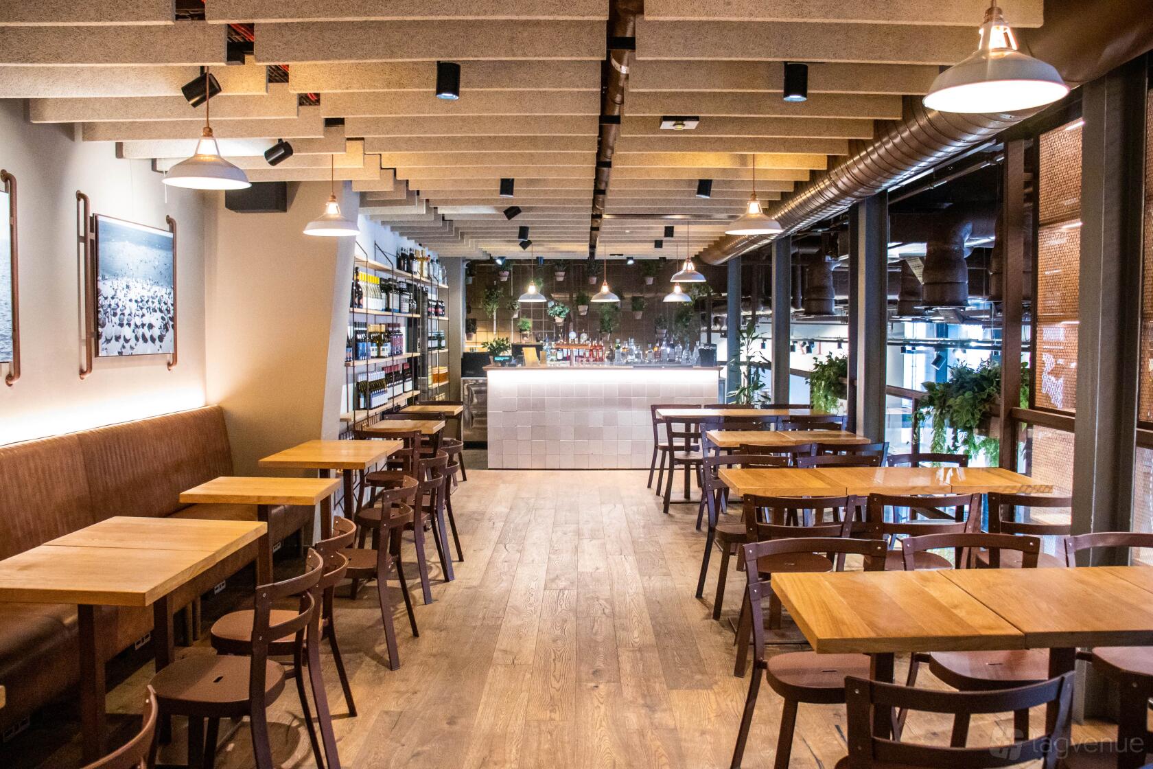 An event space in a restaurant with wooden tables, cushioned bench seating, and pendant lights at Eataly London.