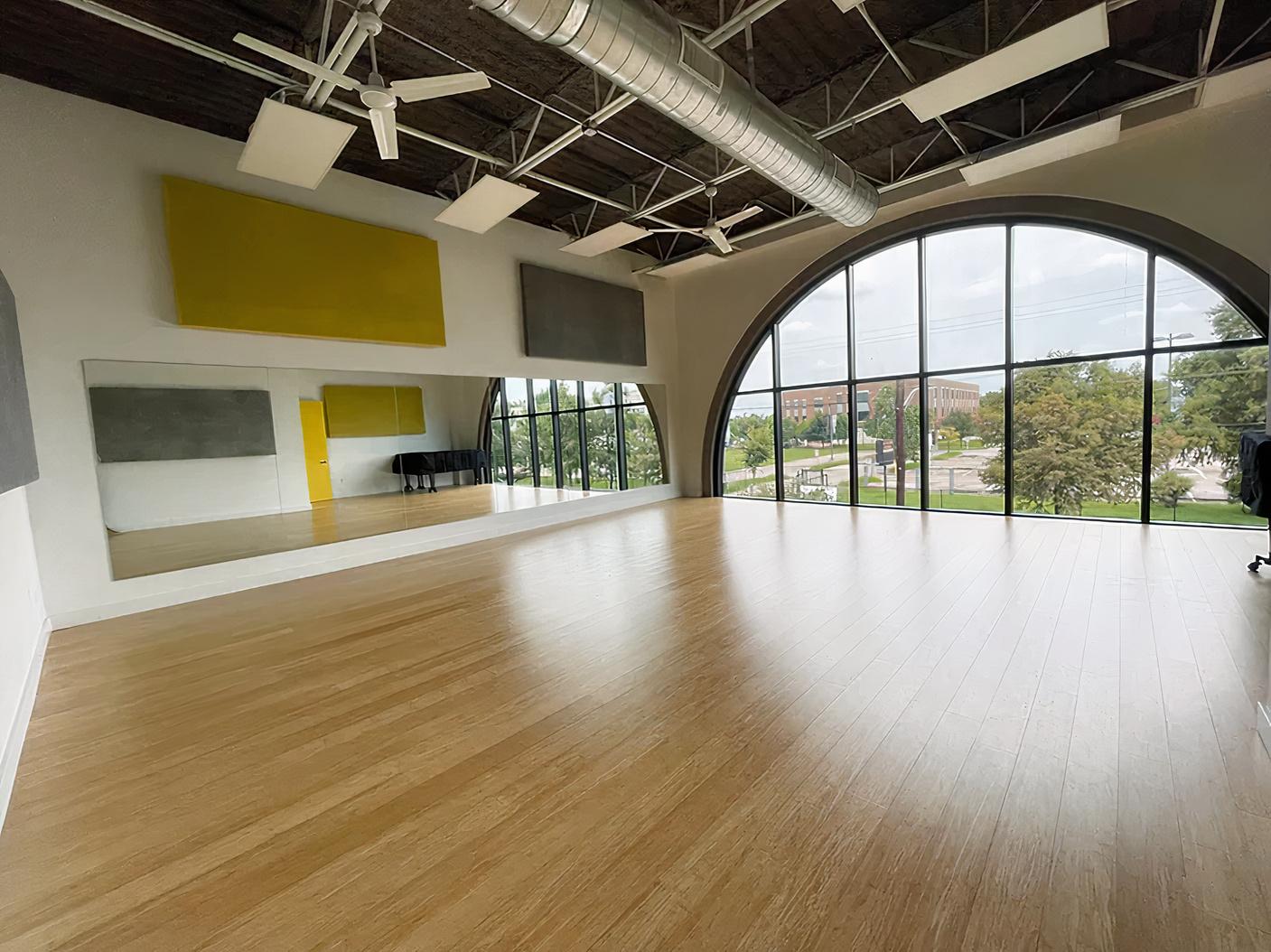 A dance studio with wood floors, wall mirrors, acoustic panels, and a large arched window at GARZA STUDIOS.