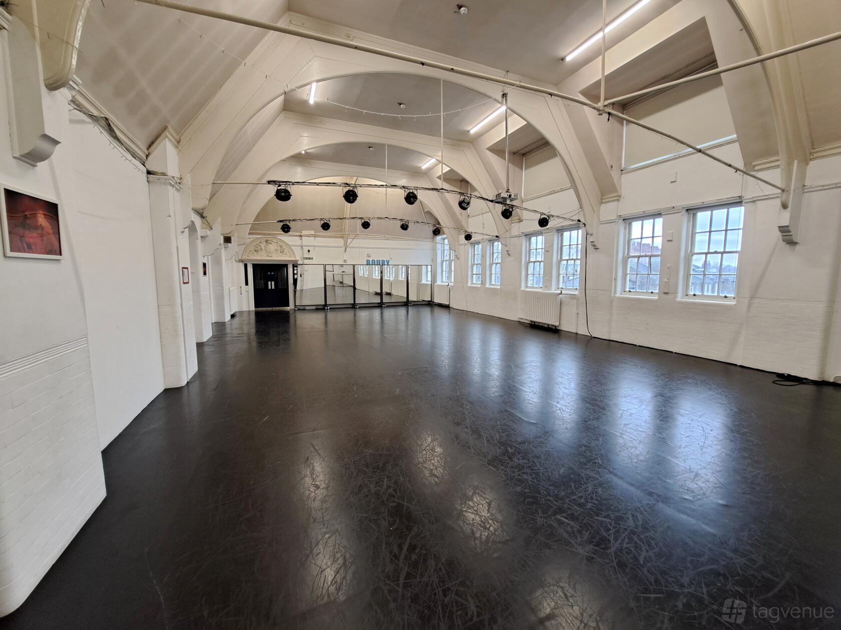 A rehearsal room with high arched ceilings, black dance floor, and large windows at The Boury Studios.