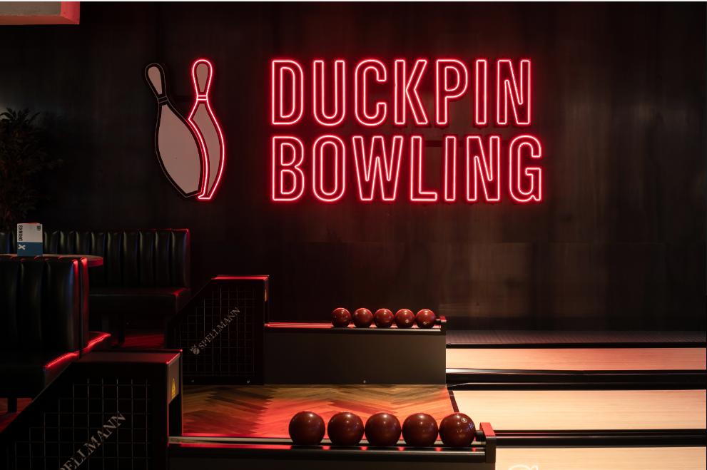 A bowling alley with duckpin lanes, red neon signage, and wooden floors at BrewDog Waterloo.