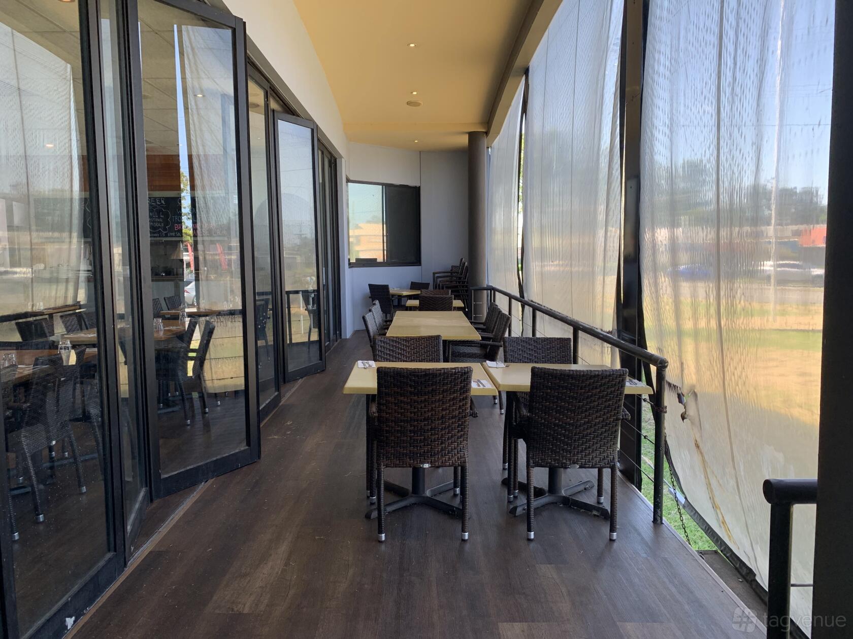 A terrace with wicker chairs, rectangular tables, and floor-to-ceiling sheer curtains at Portabella Restaurant.