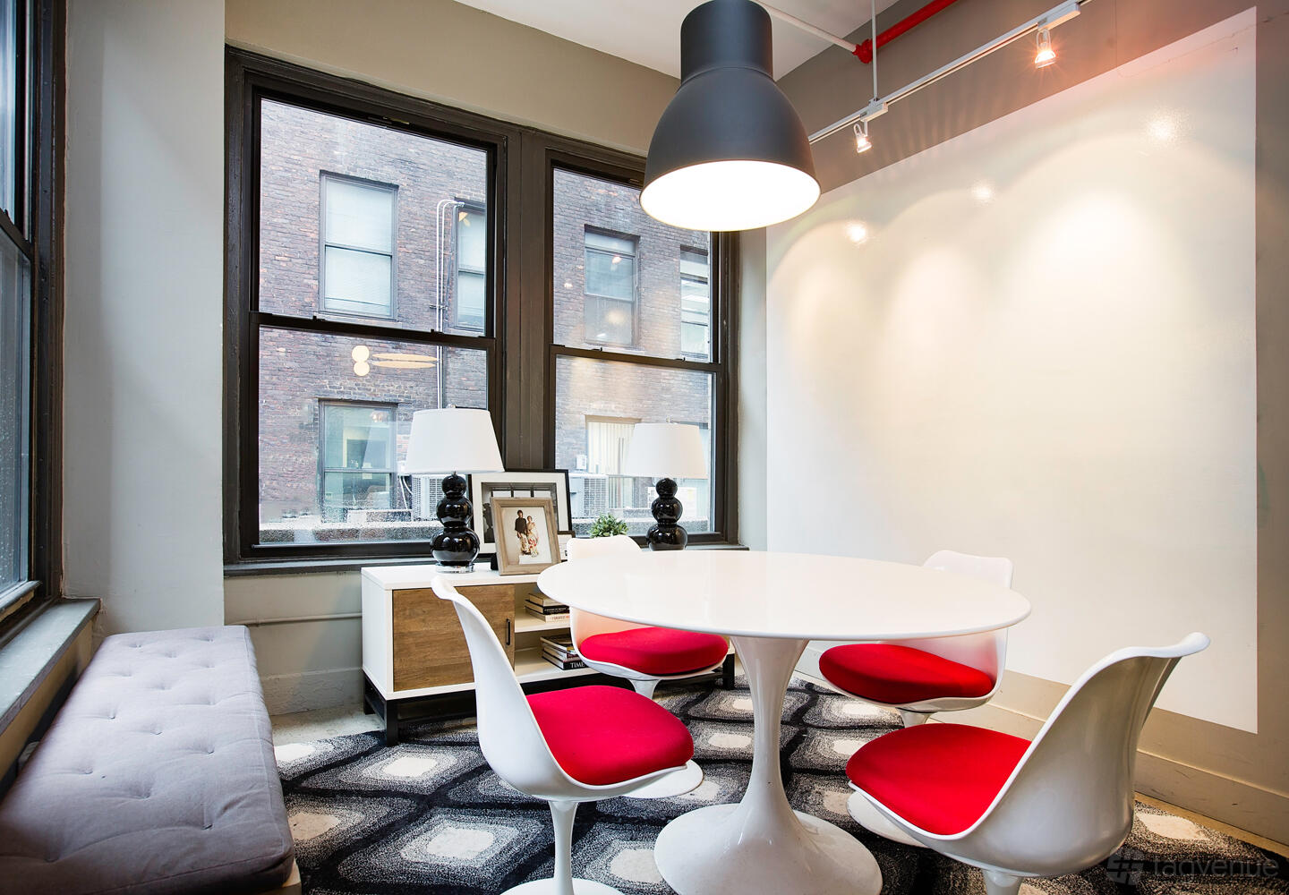 A coworking space with a round white table, red chairs, and large windows at WorkHouse NYC - Midtown.